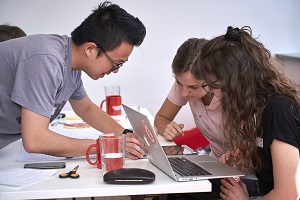 Drei junge Menschen arbeiten zusammen über einen Laptop gebeugt